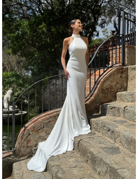 Vestido de cuello halter ajustado con espalda al aire y cola. Capa de vuelo volante con lazada en el cuello.