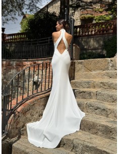 Vestido de cuello halter ajustado con espalda al aire y cola. Capa de vuelo volante con lazada en el cuello.