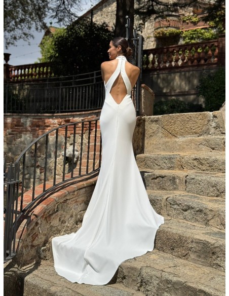 Vestido de cuello halter ajustado con espalda al aire y cola. Capa de vuelo volante con lazada en el cuello.