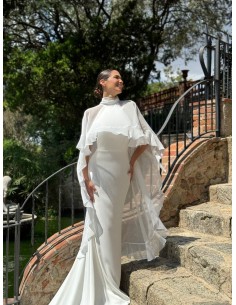 Vestido de cuello halter ajustado con espalda al aire y cola. Capa de vuelo volante con lazada en el cuello.