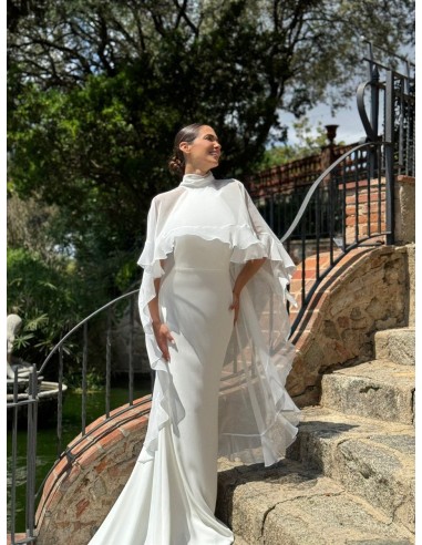 Vestido de cuello halter ajustado con espalda al aire y cola. Capa de vuelo volante con lazada en el cuello.