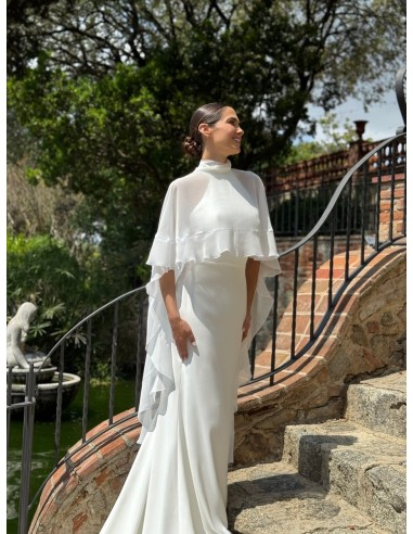 Vestido de cuello halter ajustado con espalda al aire y cola. Capa de vuelo volante con lazada en el cuello.