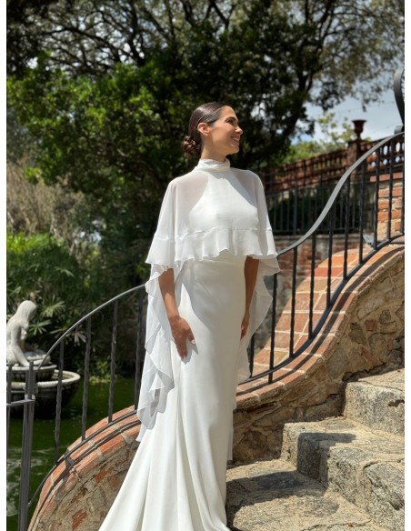 Vestido de cuello halter ajustado con espalda al aire y cola. Capa de vuelo volante con lazada en el cuello.